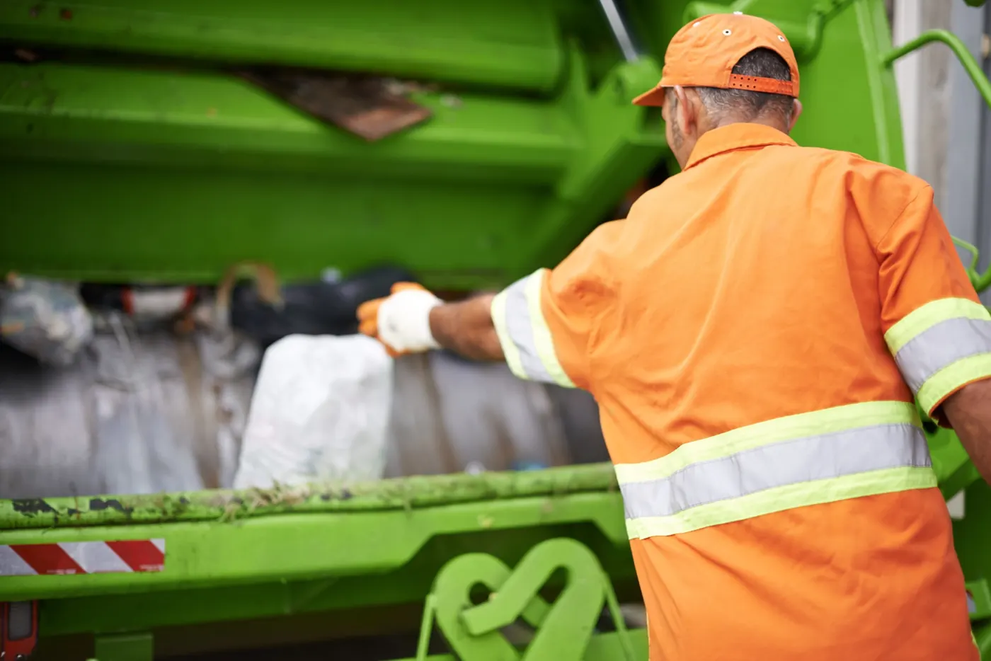 Operario cargando residuos en camión recolector verde